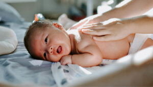 Newborn baby lying on a hospital bed while being gently massaged by a caregiver's hands on its back